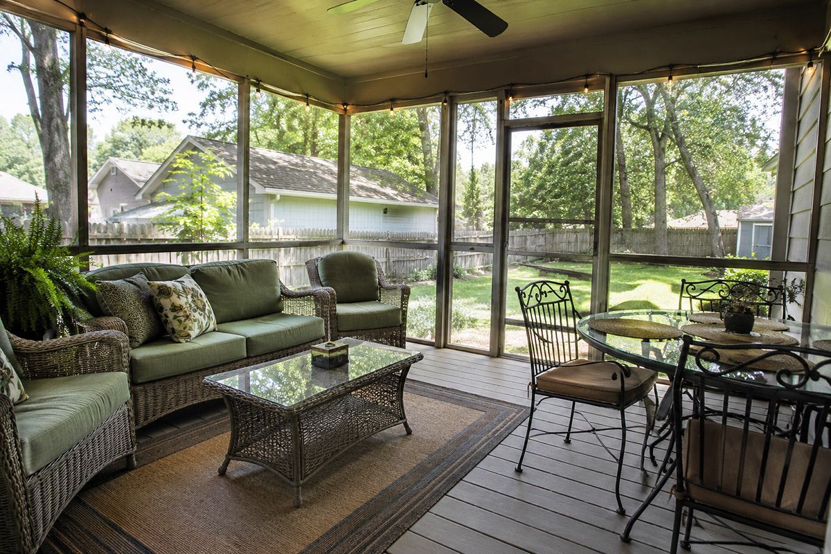Screened porch with wicker seating and table, overlooking a fenced backyard and trees.