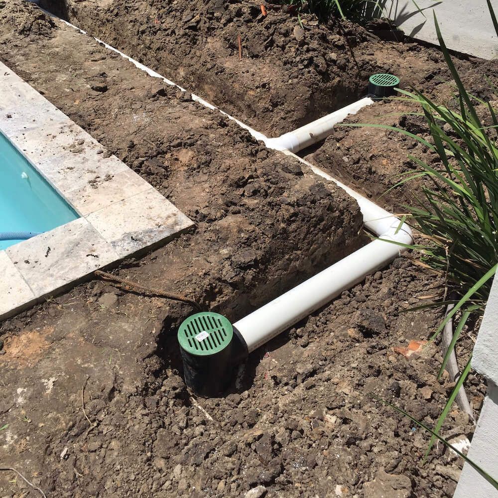 A man is working on a drainage system in the backyard of a house.