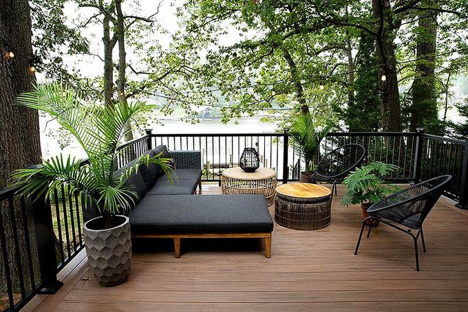 Wooden deck seating area with black lounge chairs, potted plants, and a fire pit overlooking water