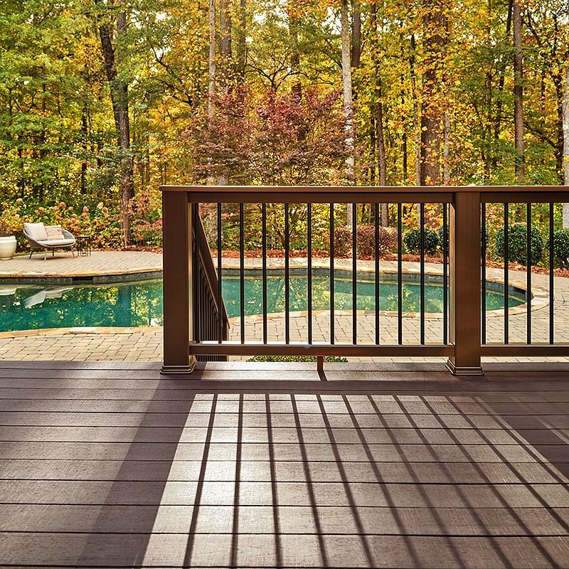 Wooden deck overlooking a turquoise pool and autumn trees, with railing casting long shadows.
