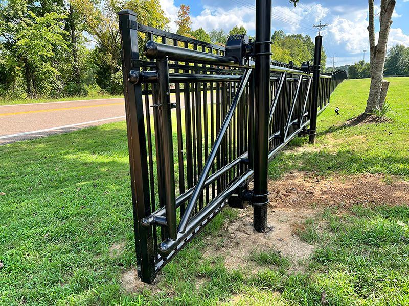 Black metal gate along a grassy roadside with trees in the background