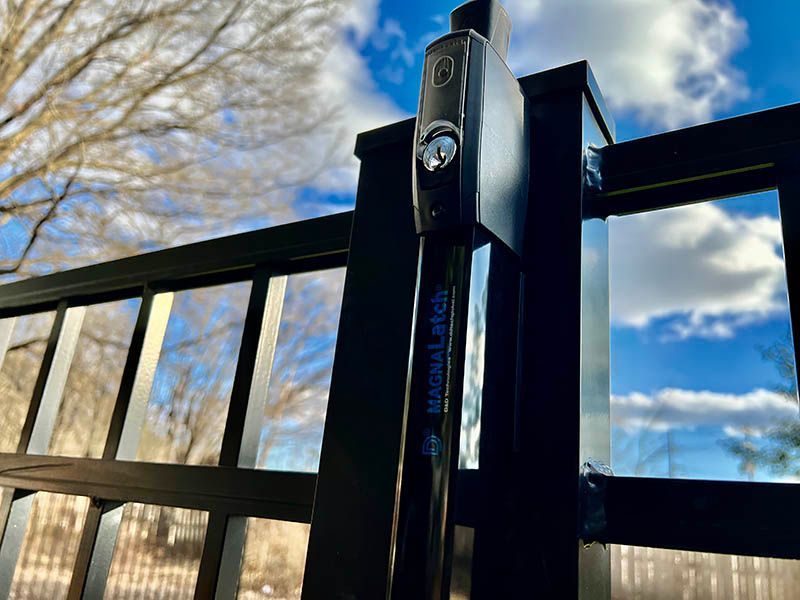 Black metal gate hinge and fence against a blue sky with clouds