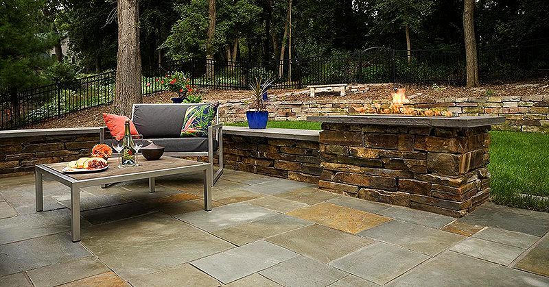 Stone patio with outdoor seating, a fire pit, and potted plants in a wooded backyard