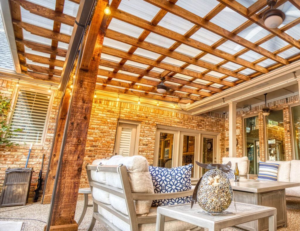 A patio with a wooden pergola and a glass roof in front of a house.