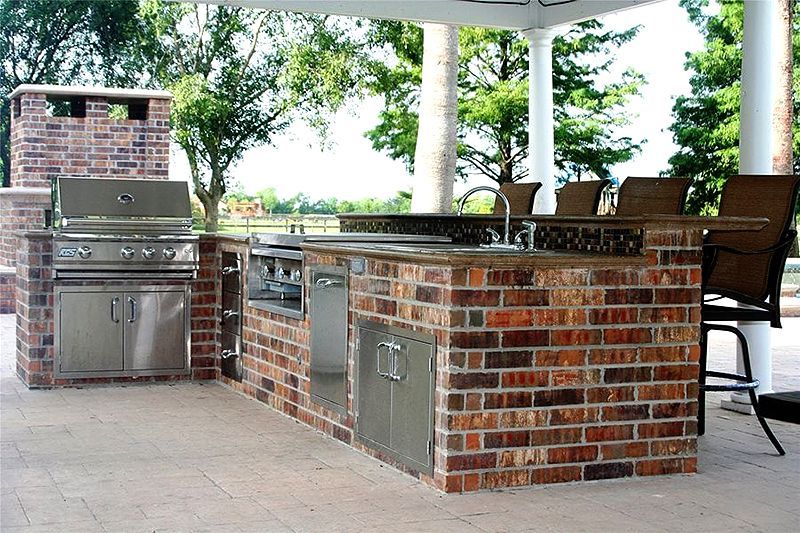 Outdoor brick kitchen and grill area under a white pavilion with stainless steel appliances and counters