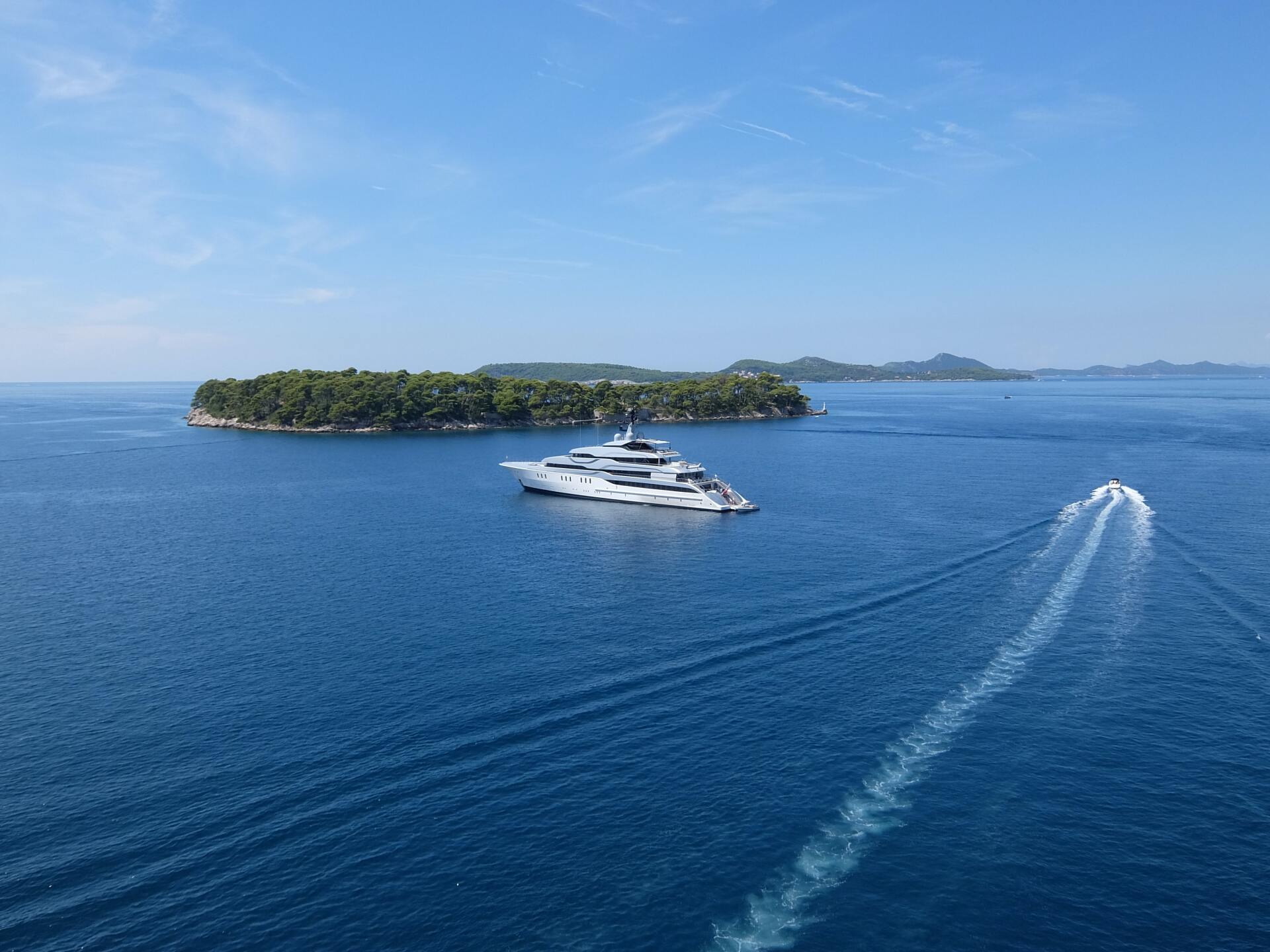 Yacht cruising across clear blue water with small island in the distance