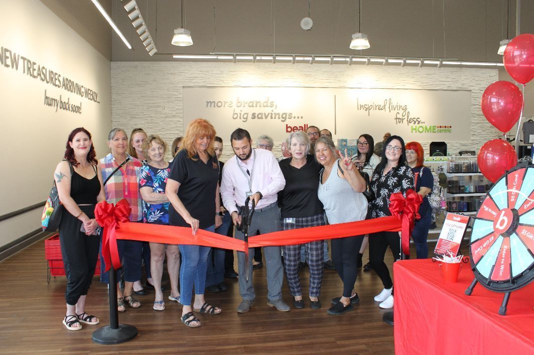 A group of people are cutting a red ribbon in a store.