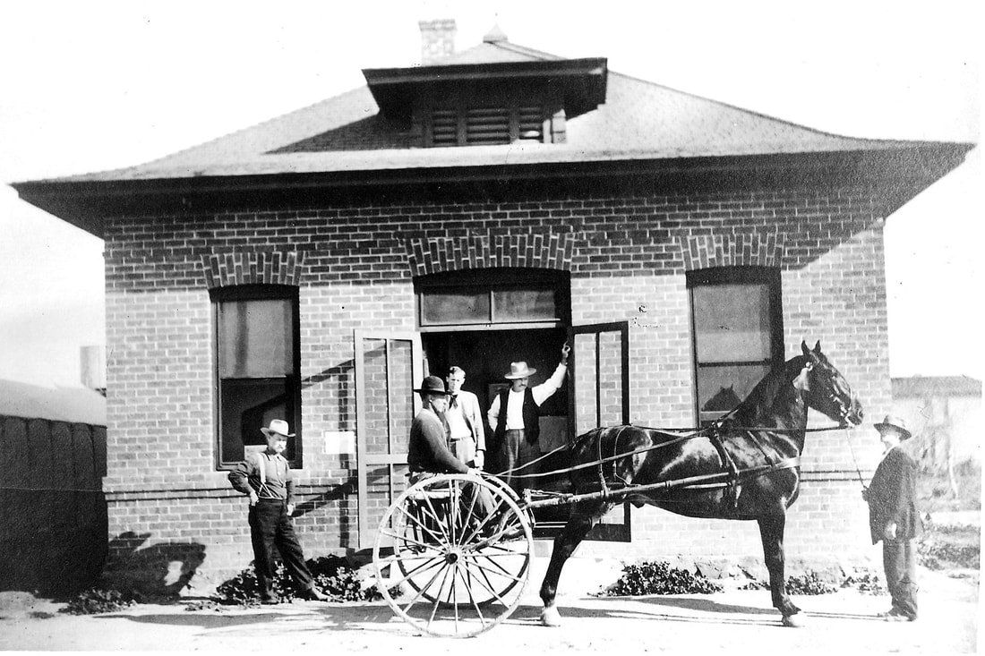 A black and white photo of a horse drawn carriage in front of a brick building.