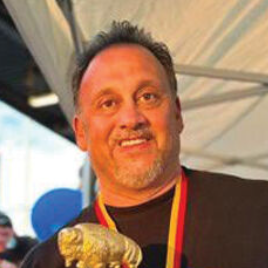 A man with a beard and mustache is smiling and wearing a black shirt.
