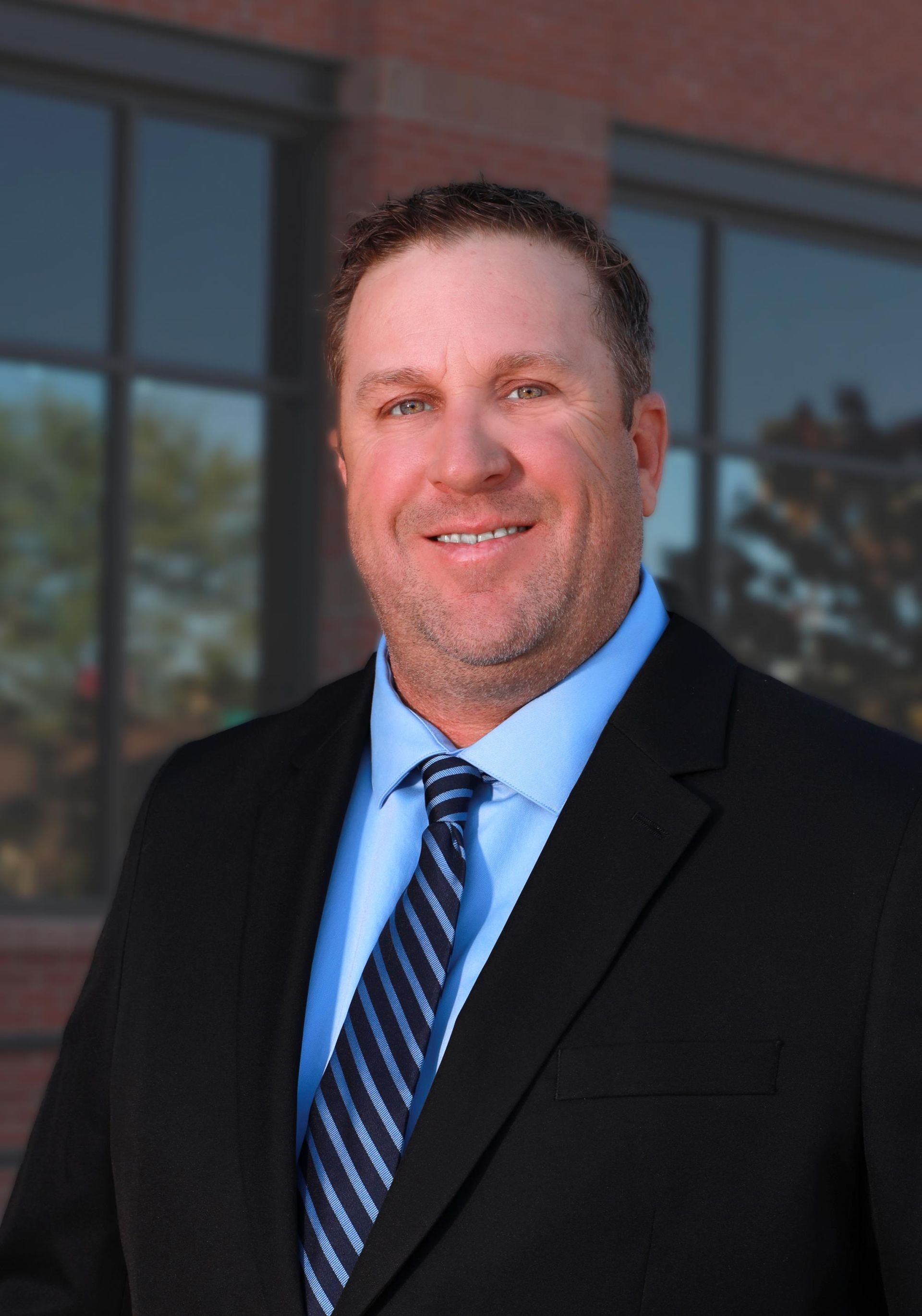 A man in a plaid shirt is standing in front of a black background.