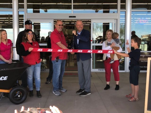 A group of people are cutting a red ribbon that says ace on it