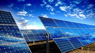 A row of solar panels against a blue sky with clouds.