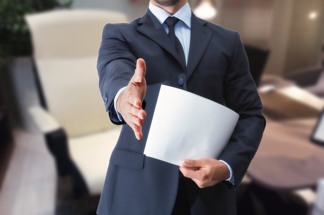 A man in a suit and tie is holding a piece of paper and reaching out to shake someone 's hand.