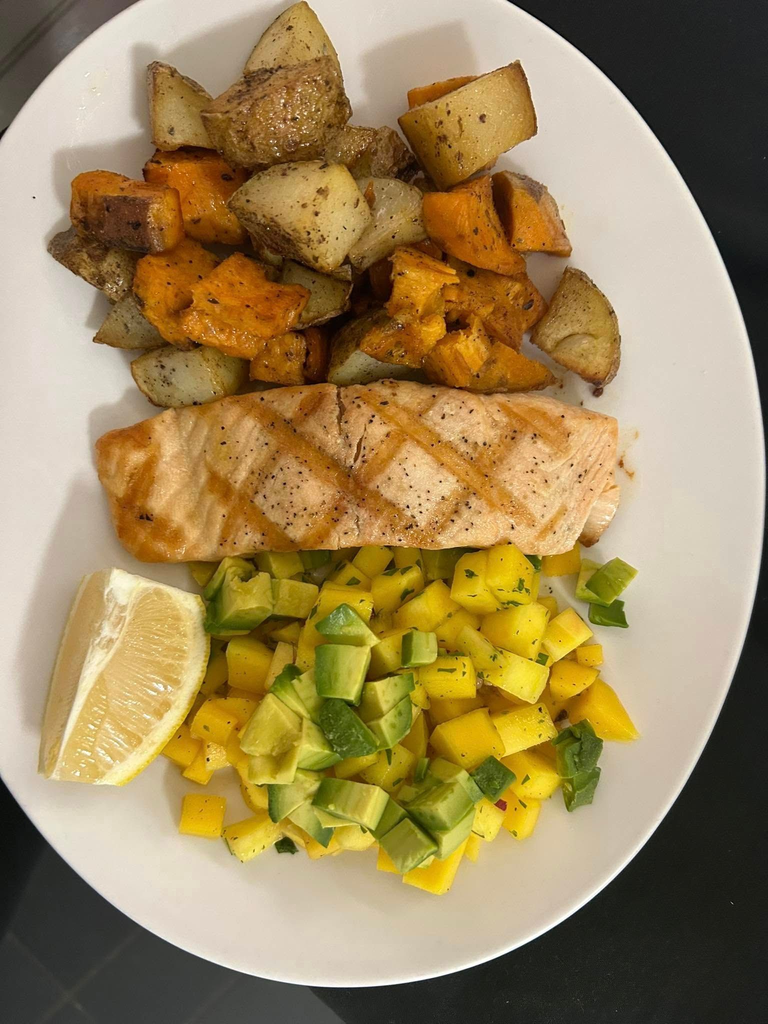 A white plate topped with salmon , potatoes and avocado.
