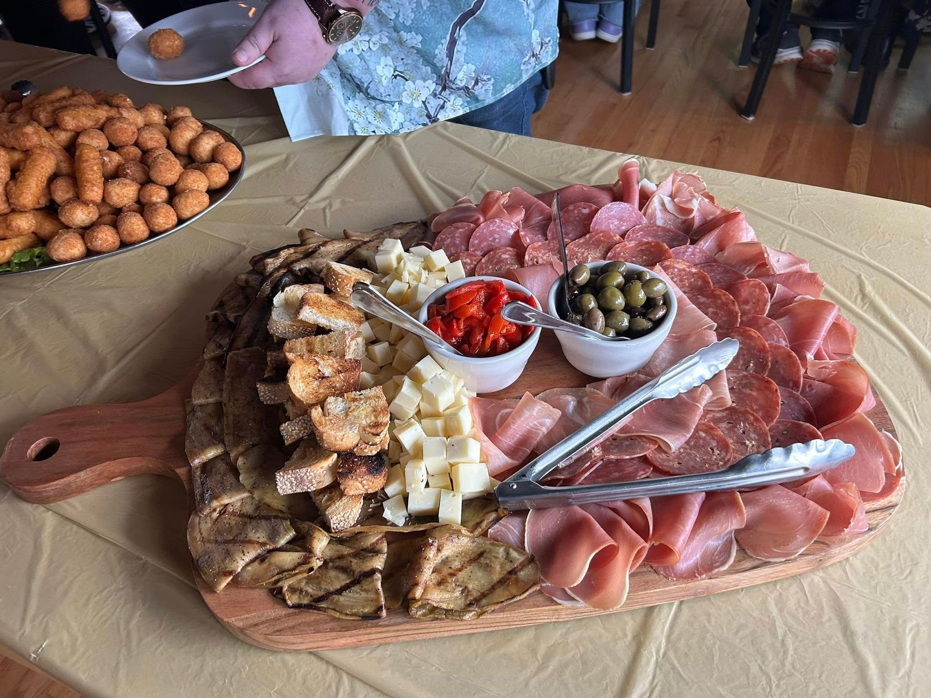 A wooden cutting board filled with meat and cheese on a table.