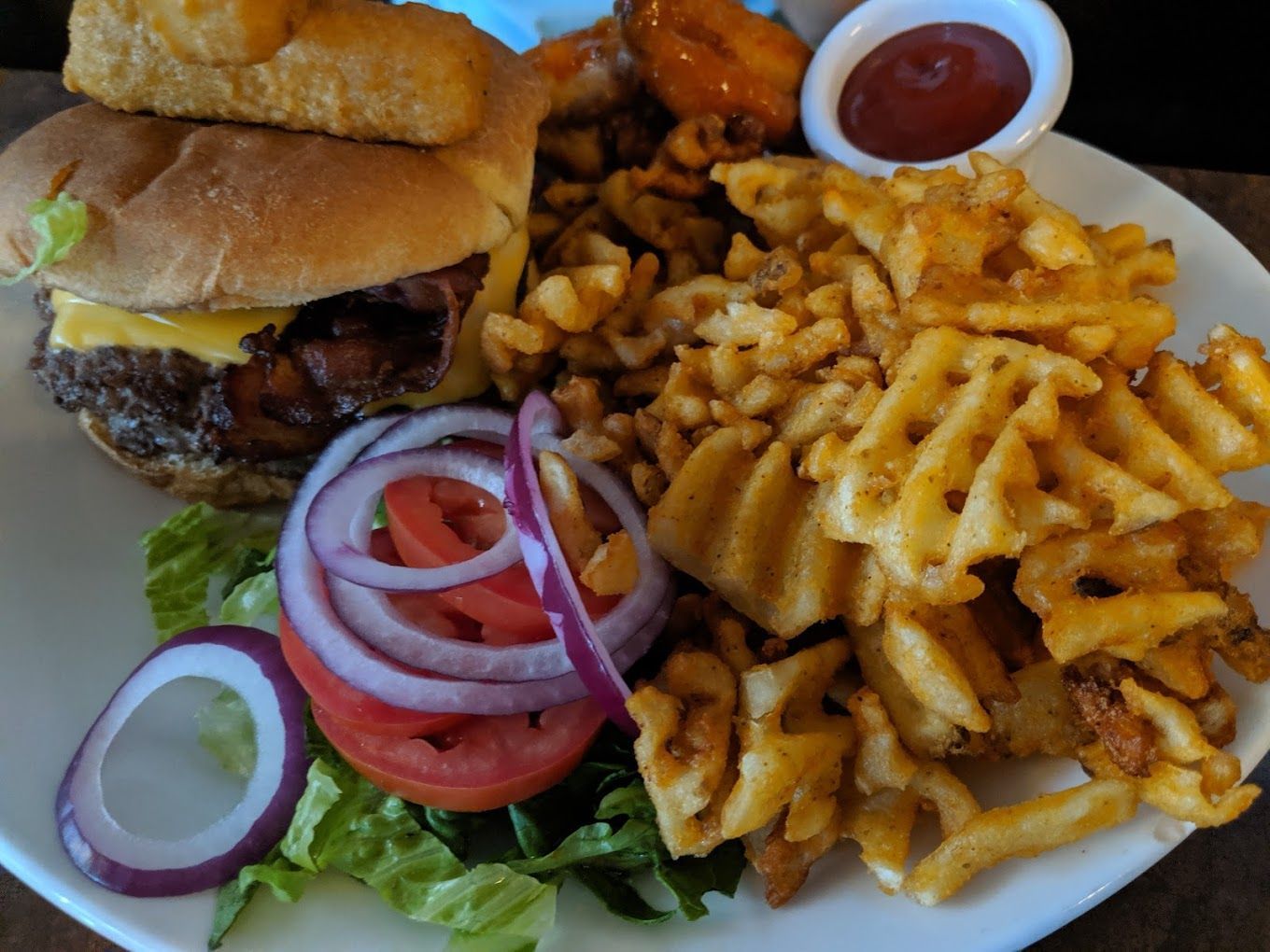 A white plate topped with a hamburger , waffle fries , and chicken wings.