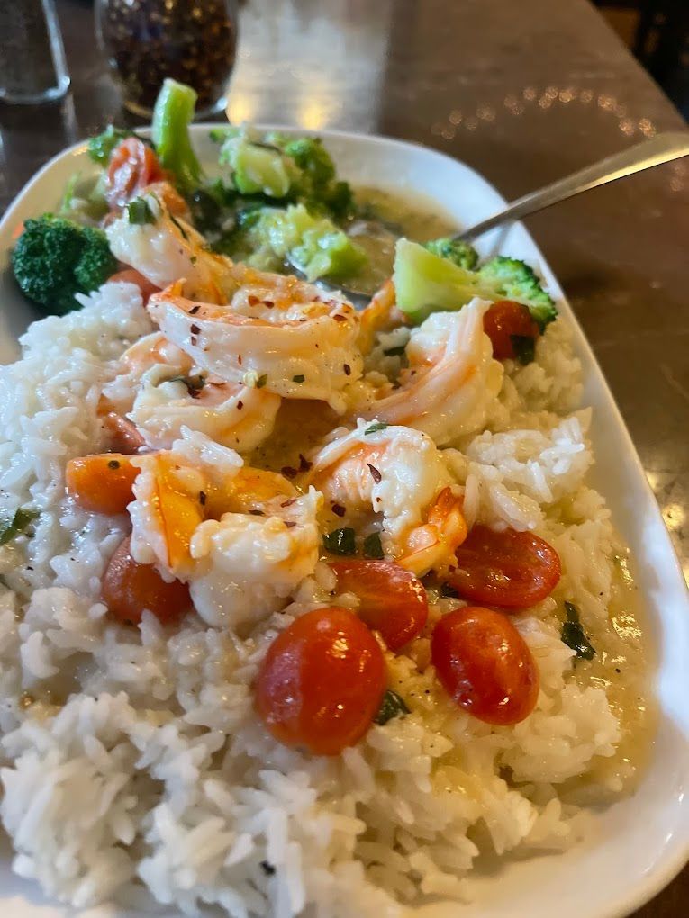 A plate of food with shrimp , rice , broccoli and tomatoes on a table.