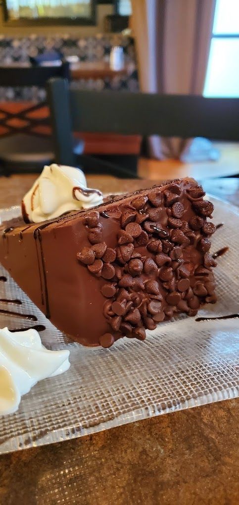 A piece of chocolate cake with whipped cream and chocolate chips on a plate on a table.