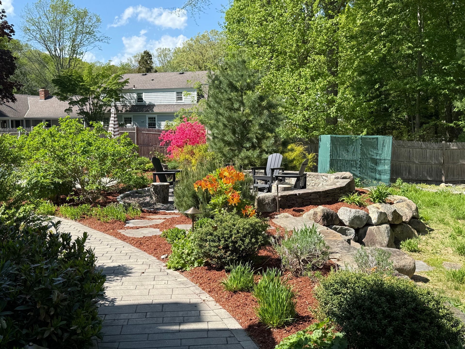 A residential yard with freshly mowed grass, a small tree, a blue trash bin, and an open attached garage on a sunny day.