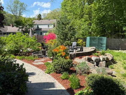 A residential yard with freshly mowed grass, a small tree, a blue trash bin, and an open attached garage on a sunny day.