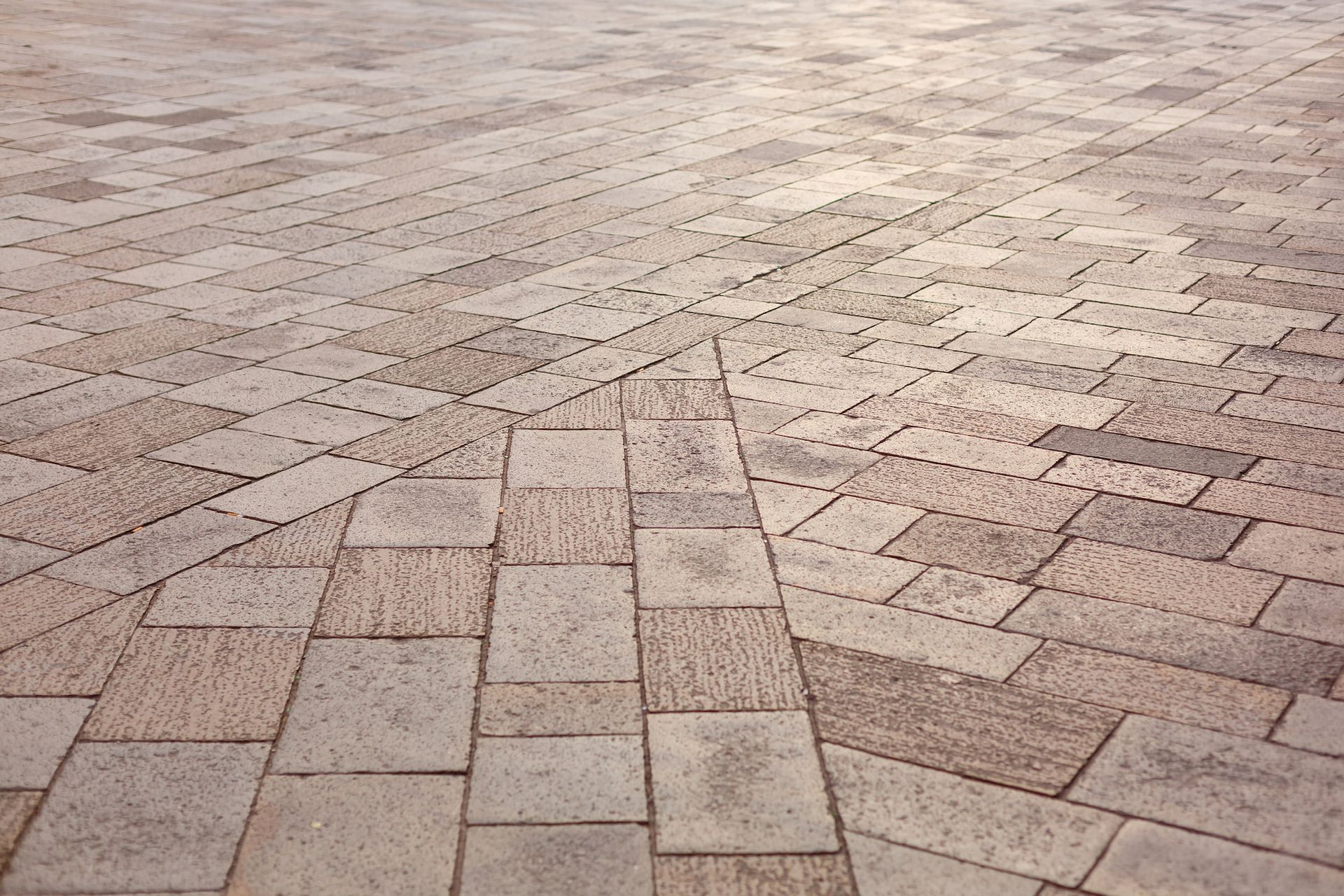 A close-up view of textured, beige and light brown rectangular paving stones arranged in a geometric, angled pattern.