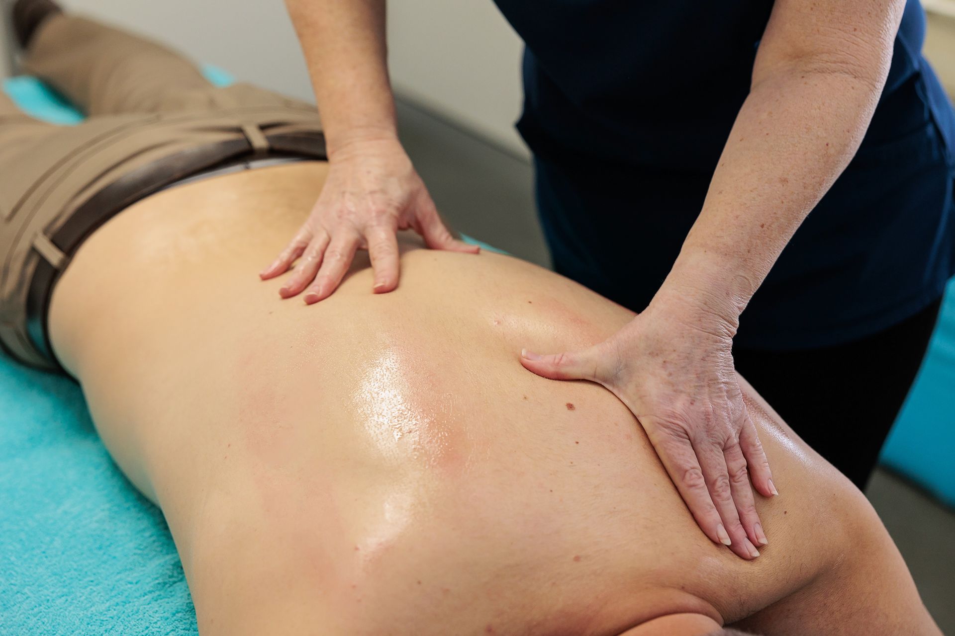 Person receiving a back massage with visible oil on a light-skinned back; masseuse's hands applying pressure.