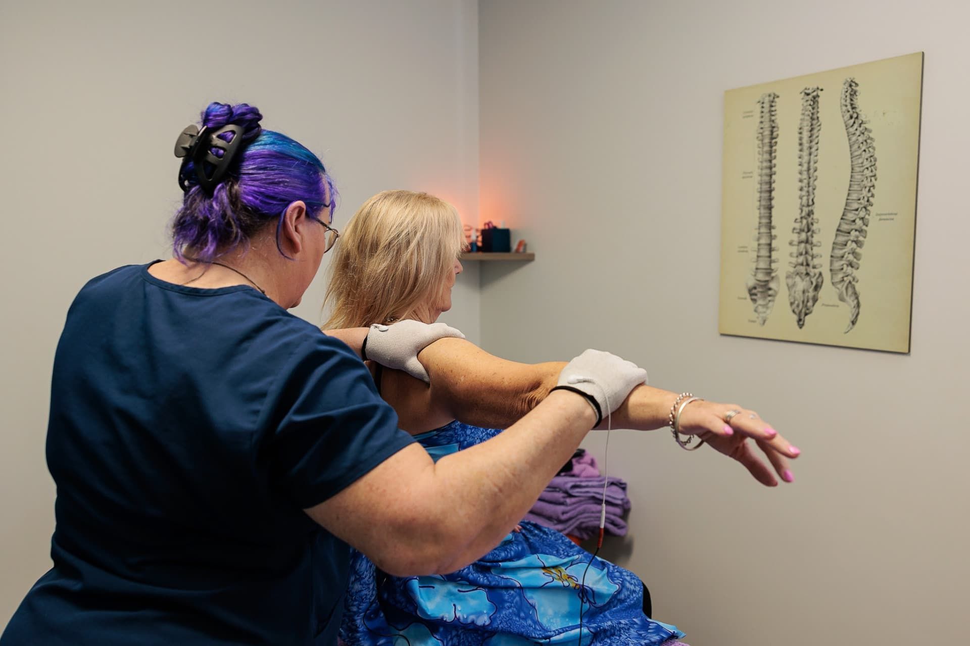 Chiropractor Adjusting a Woman's Shoulder in A Room. a Spine Chart Hangs on The Wall — Grays Chiropractic & Wellness In Paget, QLD