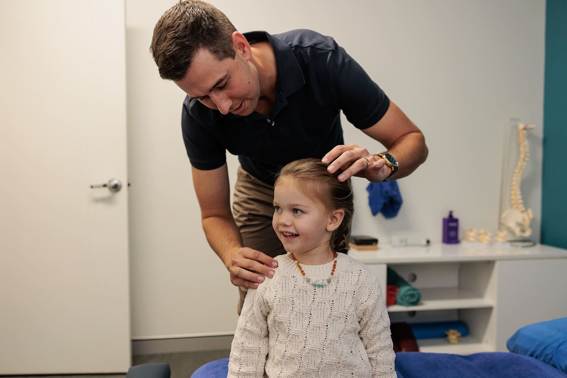 Man Examining a Smiling Young Girl's Posture in A Doctor's Office — Grays Chiropractic & Wellness In Marian, QLD