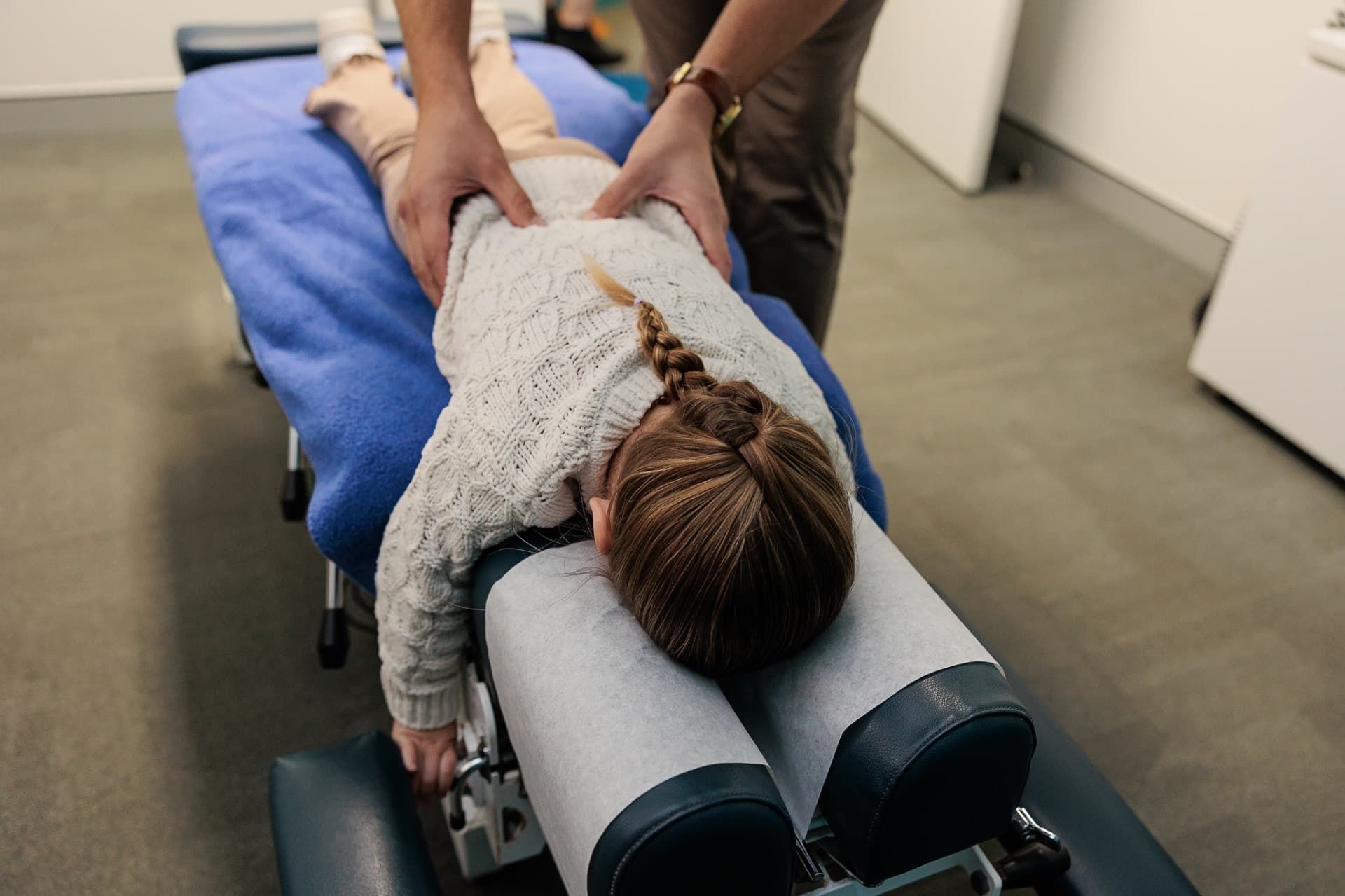 A Child Receiving a Chiropractic Adjustment, Lying on A Table with A Practitioner's Hands on Their Back — Grays Chiropractic & Wellness In Paget, QLD