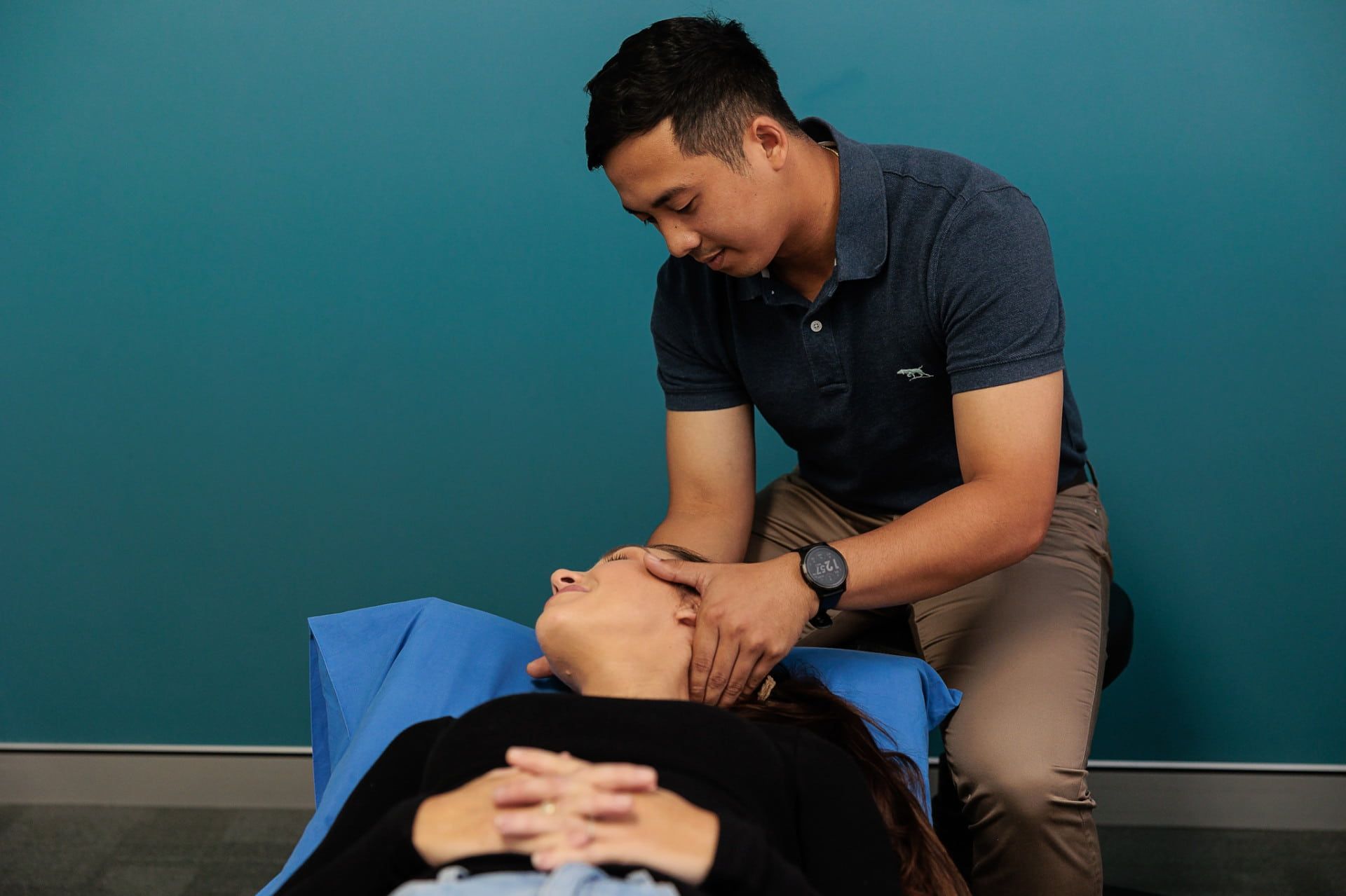 Man Performing Facial Massage on A Woman Lying Down, Teal Wall Backdrop — Grays Chiropractic & Wellness In Ooralea, QLD