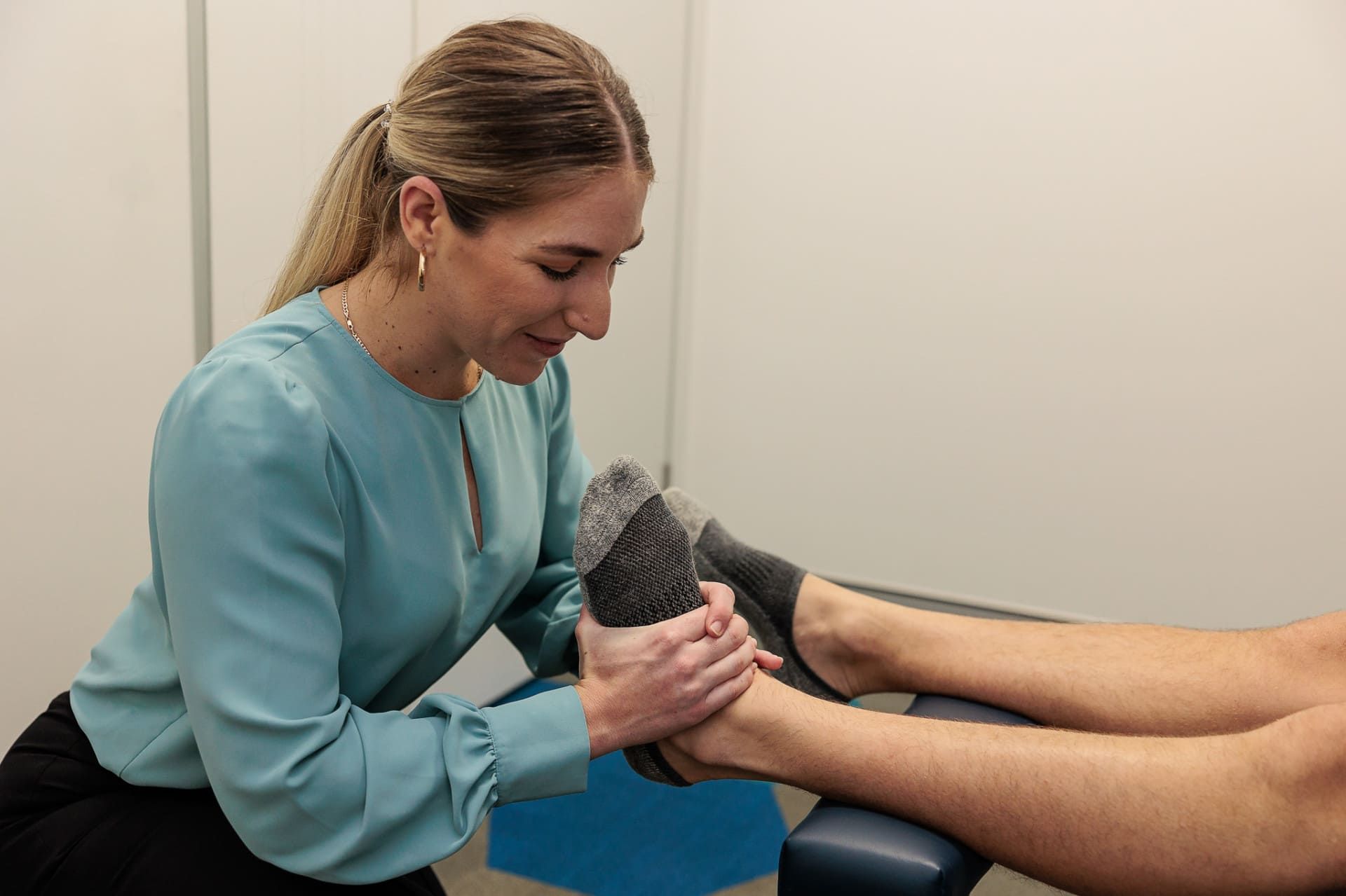 A Woman in A Blue Shirt Examines a Patient's Foot in A Clinic — Grays Chiropractic & Wellness In Walkerston, QLD