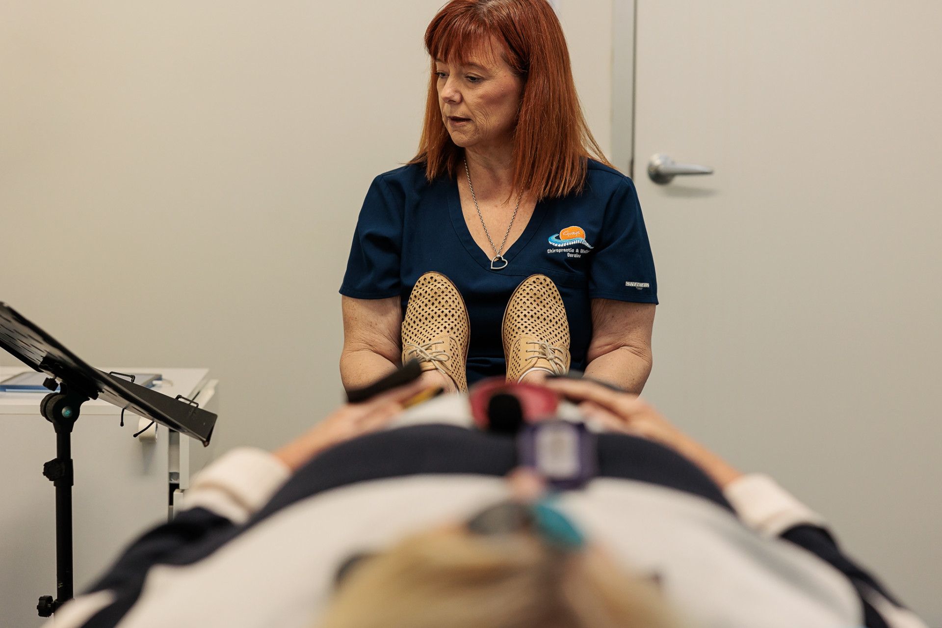 Woman in Scrubs Examining Patient Lying on A Table; Medical Equipment in Frame — Grays Chiropractic & Wellness In Ooralea, QLD