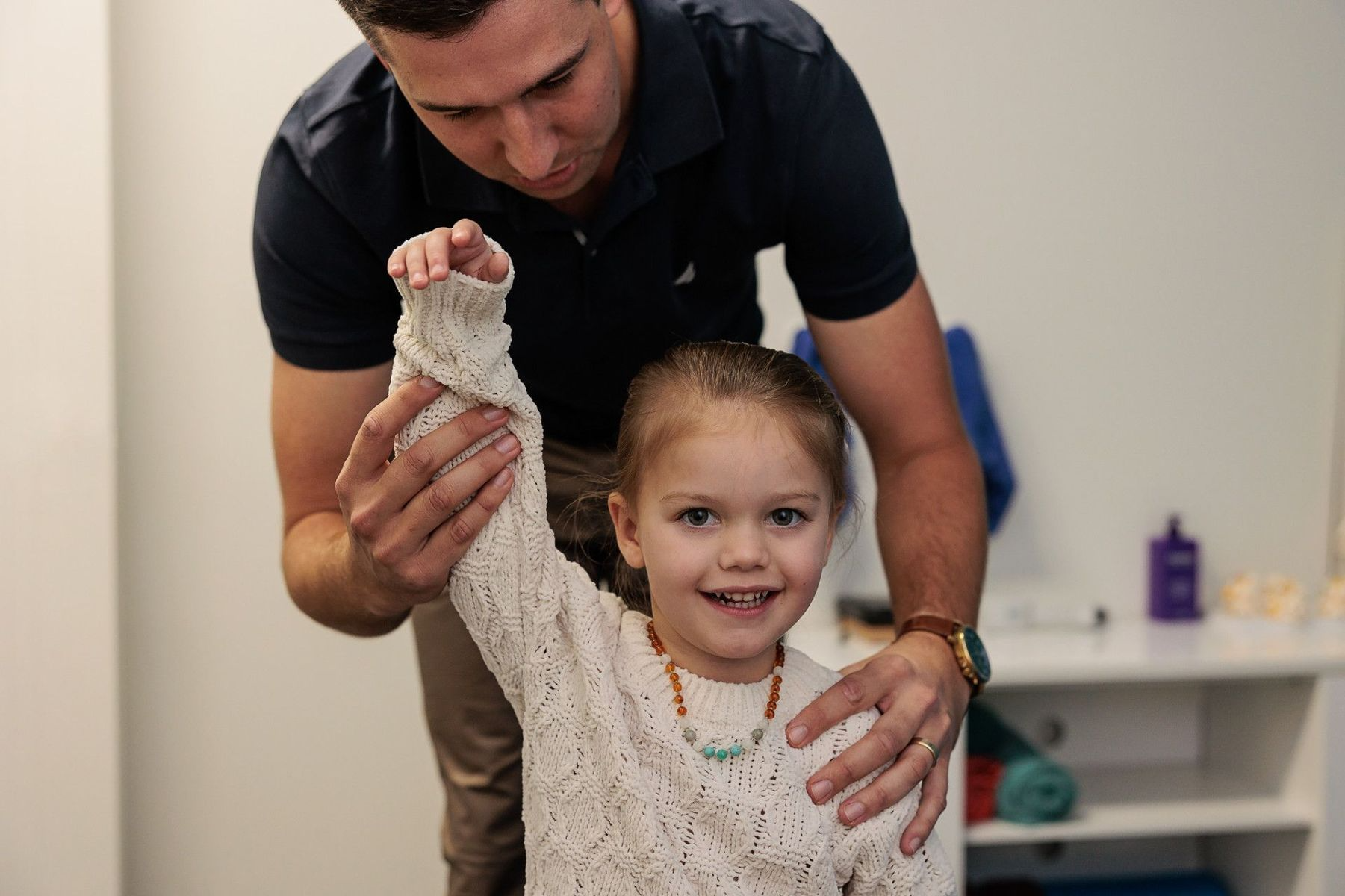 Man Assisting a Smiling Girl Raising Her Arm in A Clinical Setting — Grays Chiropractic & Wellness In Ooralea, QLD