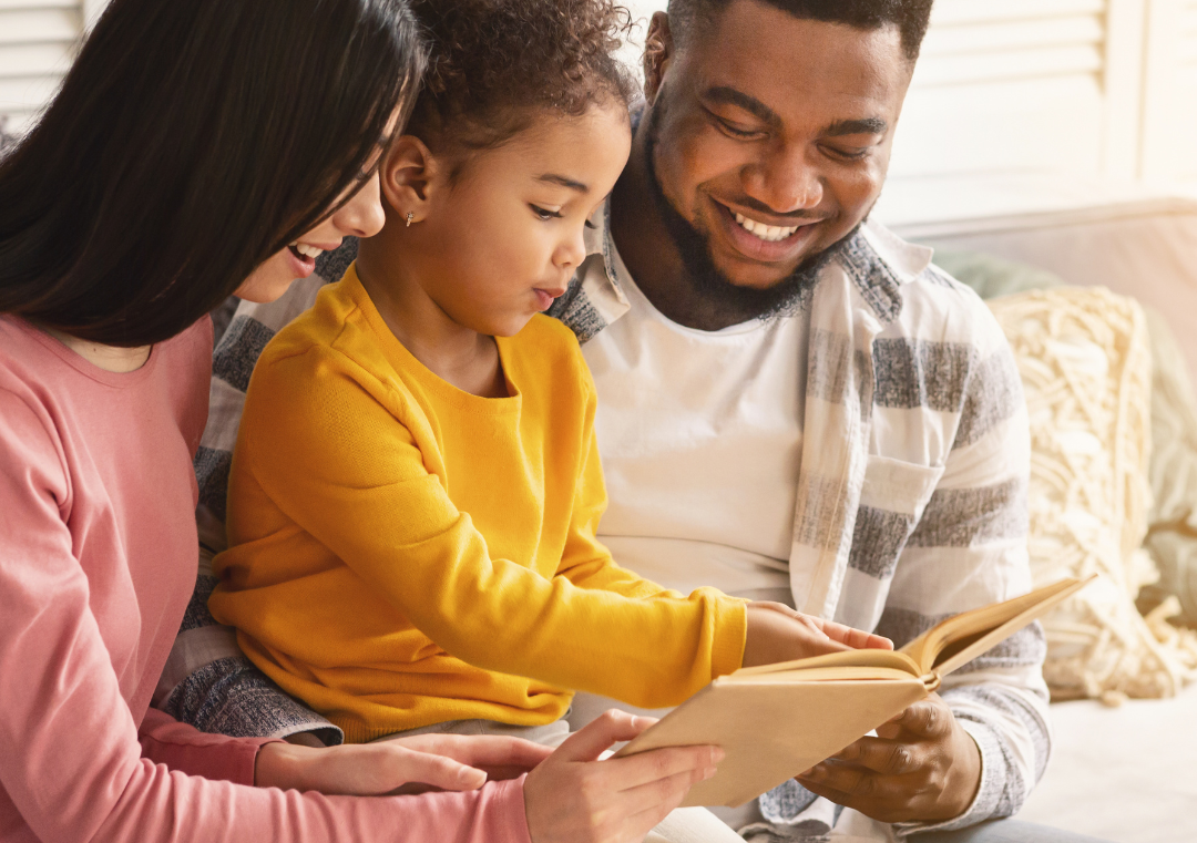 A family is sitting on a couch reading a book together.