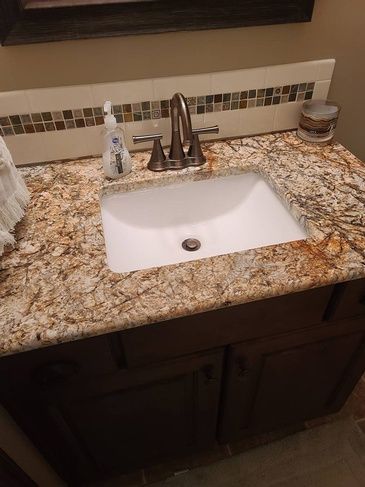 A bathroom sink with a granite counter top and a soap dispenser.