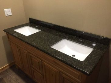 A bathroom vanity with two sinks on a granite counter top.