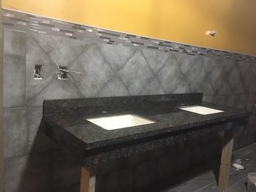 A bathroom with two sinks and a tiled wall.