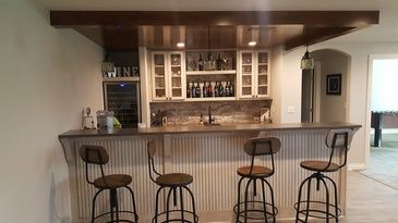 A bar with stools and a wine cooler in a basement.