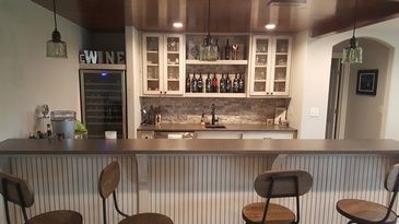 A kitchen with a bar and chairs and a wine cooler.