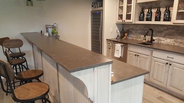 A kitchen with a long counter and stools and bottles on the wall.