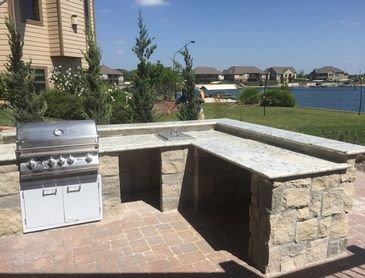 A grill is sitting on a brick patio next to a lake.
