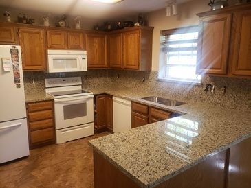 A kitchen with granite counter tops , wooden cabinets , white appliances , and a refrigerator.