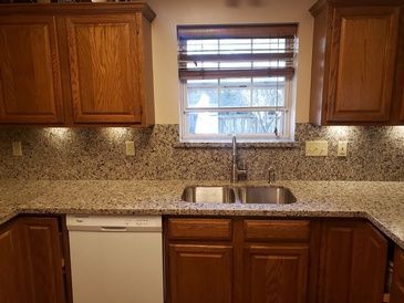 A kitchen with a sink , dishwasher , cabinets and a window.