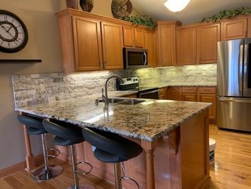 A kitchen with wooden cabinets , granite counter tops , stainless steel appliances and a clock on the wall.