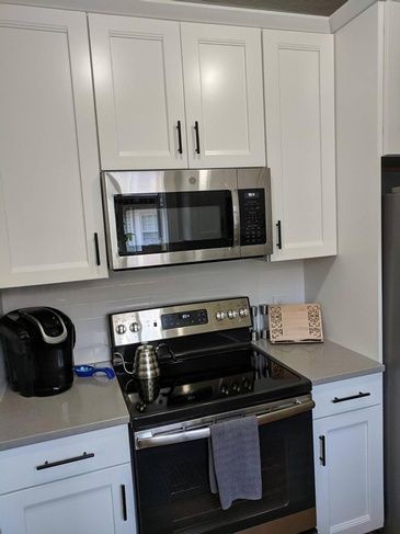A kitchen with a stove , oven , microwave and white cabinets.