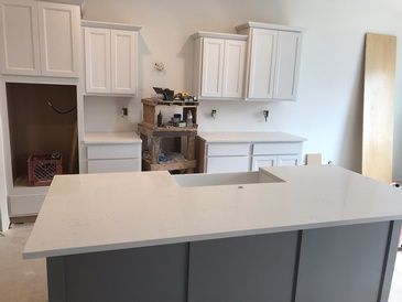 A kitchen with white cabinets and a large island with a sink.