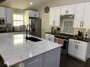 A kitchen with white cabinets , black counter tops , stainless steel appliances and a large island.