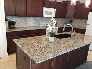 A kitchen with granite counter tops , wooden cabinets , a sink , and a microwave.