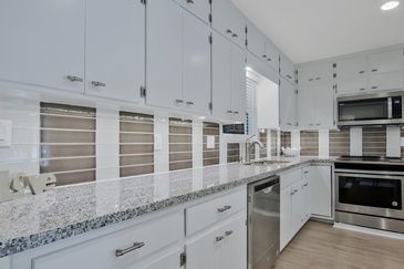 A kitchen with white cabinets , granite counter tops , stainless steel appliances and a sink.