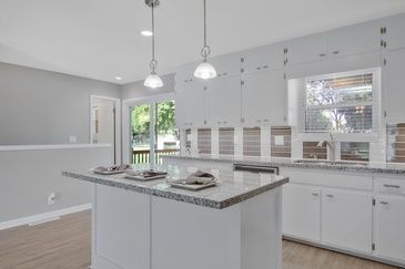 A kitchen with white cabinets , granite counter tops , and a large island.